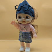Doll wearing a pink shirt with a cartoon character and a denim hat with glasses on a beige background